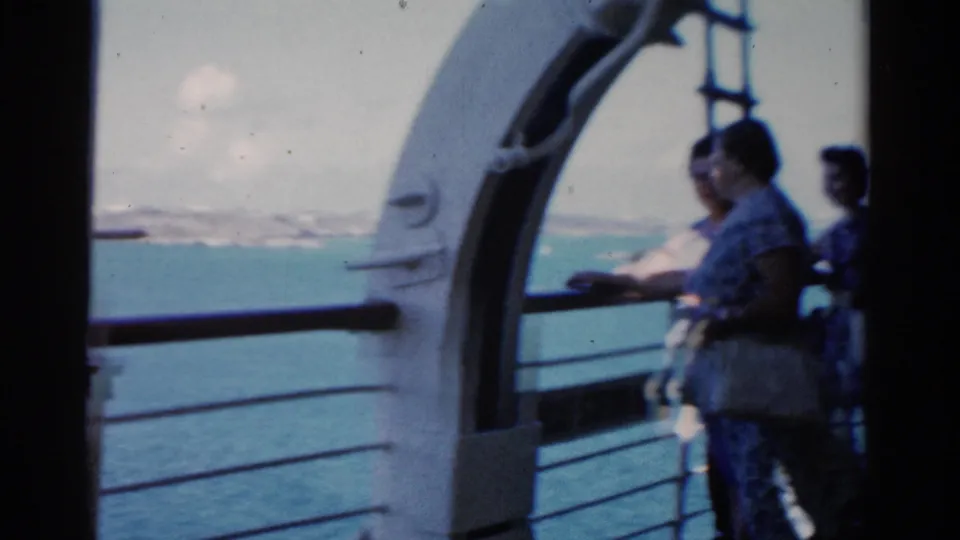 A passenger in summer clothing stands at the railing while others remain nearby on a Florida ship deck in 1975 footage.