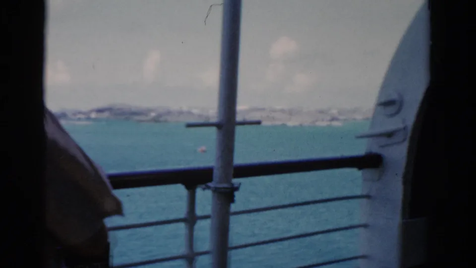 The camera looks past the ship railing toward blue water, a hazy shoreline, and deck structure in 1975 Florida footage.