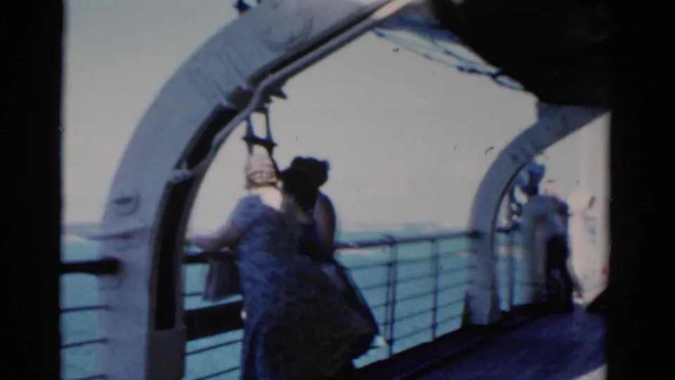 Passengers move along the ship deck beneath curved white supports, with open water visible beyond the rail in 1975 Florida footage.