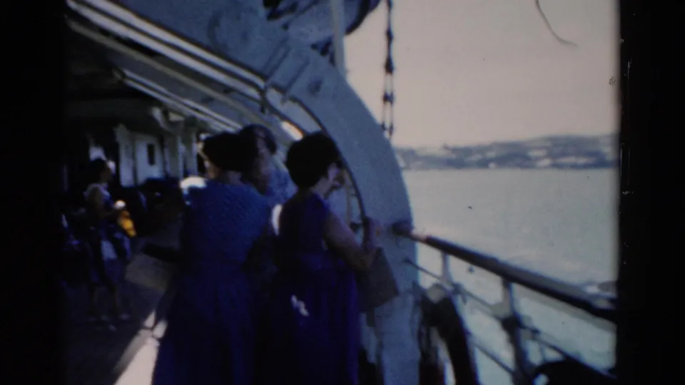 A handheld 8mm view shows adults on a Florida boat deck in 1975, with water and shoreline visible past the rail.