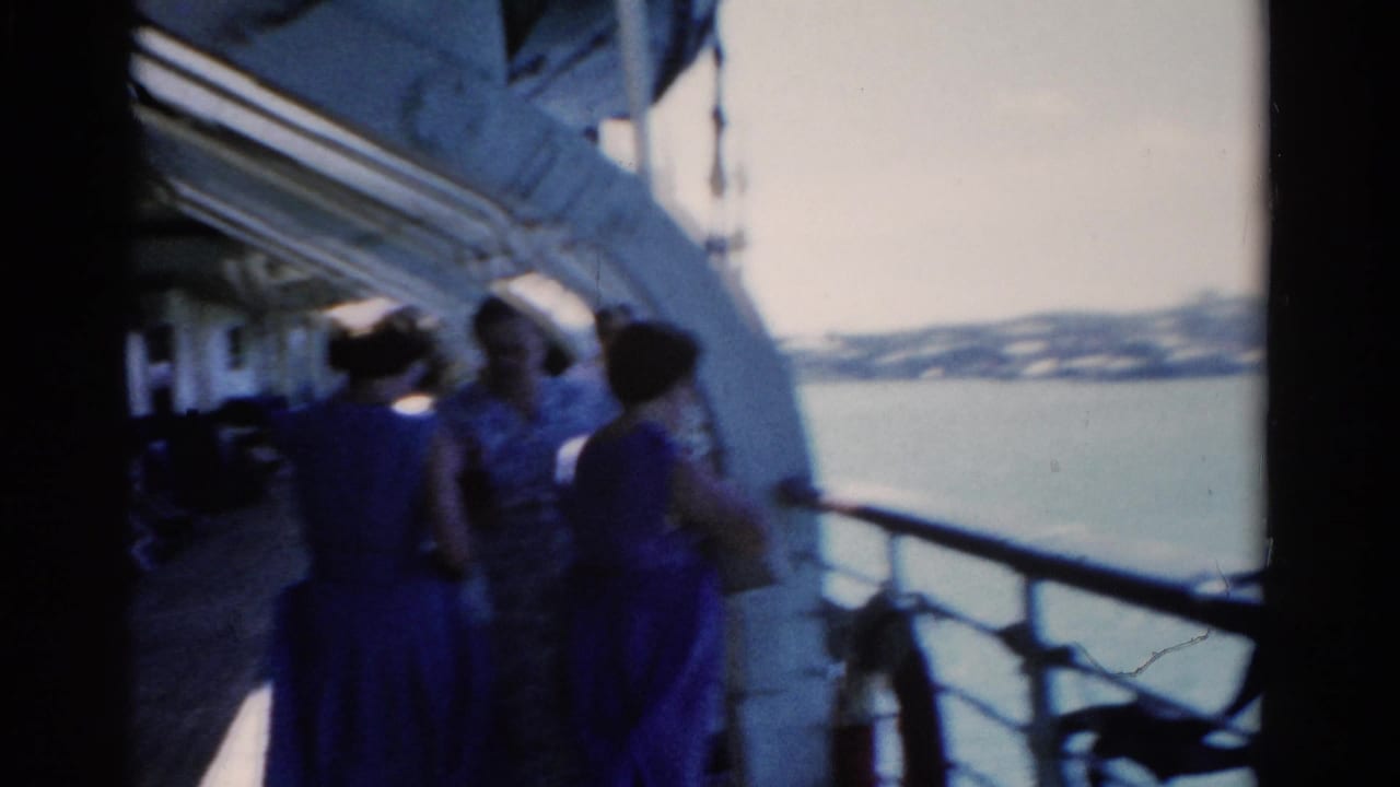 Passengers in 1970s clothing stand on a Florida cruise ship deck, seen in soft 8mm color beside the water.