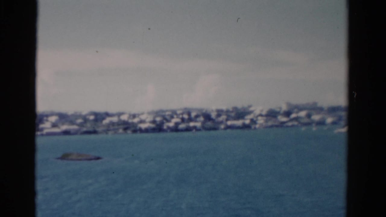 1975 Florida 8mm frame showing open blue water, a small islet, and a soft distant shoreline viewed from offshore.