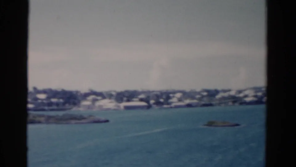 1975 Florida coastal home-movie frame showing islets in blue water with a distant low shoreline and soft waterfront buildings.