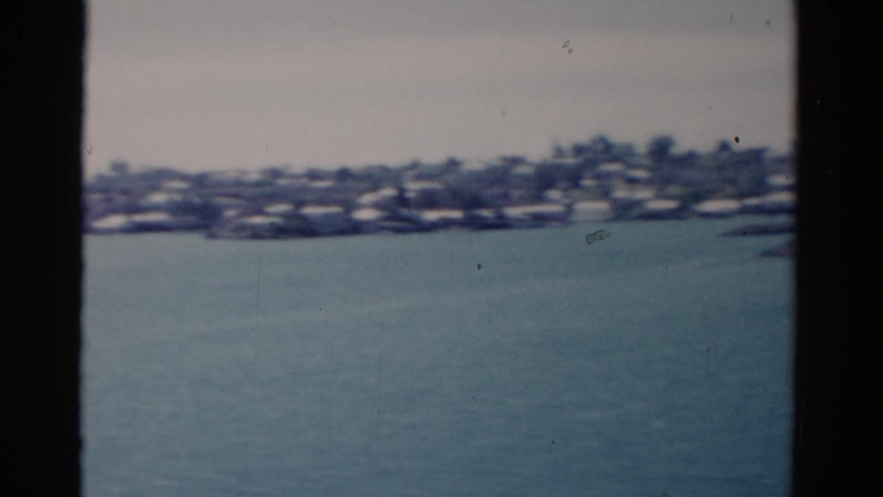 Distant shoreline and houses across blue water, framed by dark boat or window edges.