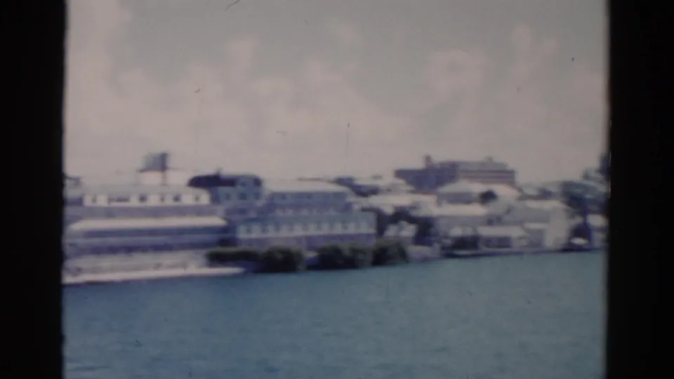 Soft 1975 Florida home-movie frame showing a waterfront building complex and shoreline across calm water.