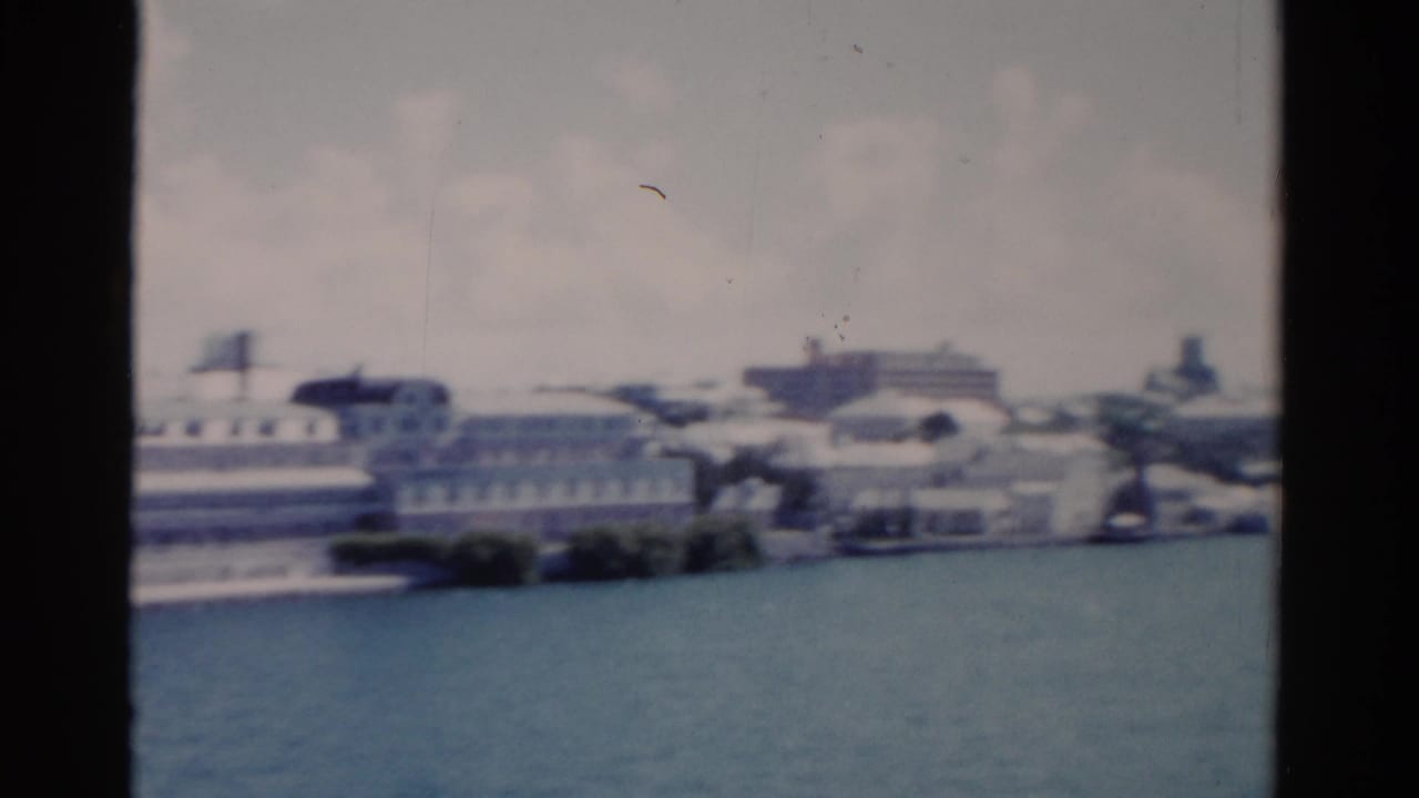 Soft 8mm view of white waterfront buildings beside blue-green water.