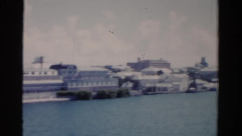 1975 Florida 8mm frame showing pale shoreline buildings and harbor water under a hazy bright sky.