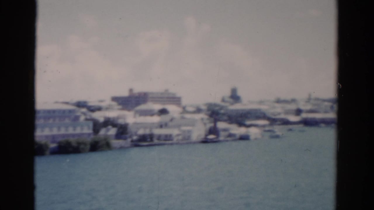 1975 Florida coastal view with pale buildings, harbor water, and small distant boats in soft focus.