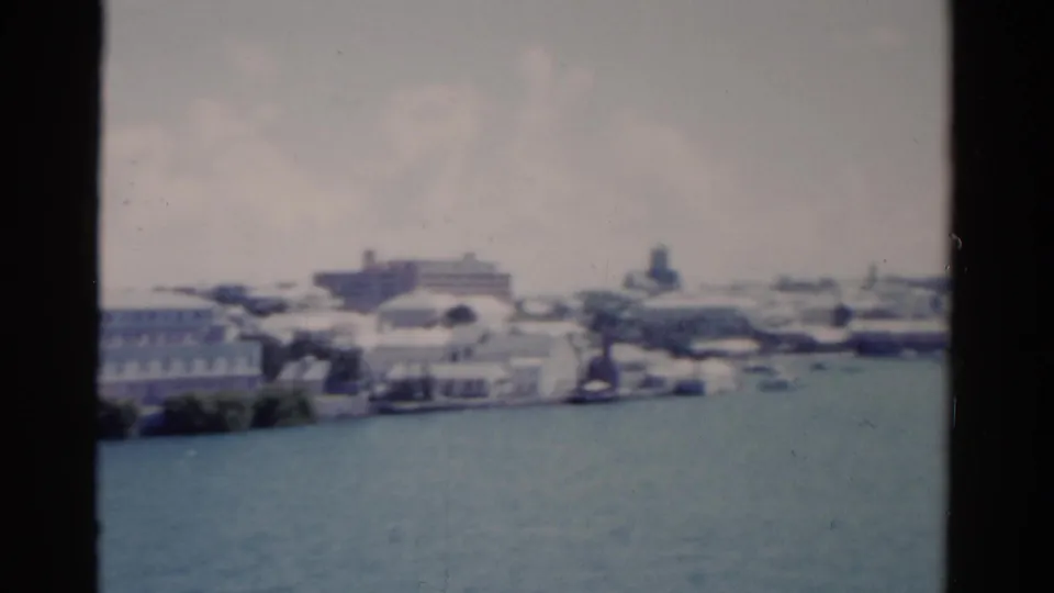 1975 Florida coastal view with pale buildings, harbor water, and small distant boats in soft focus.