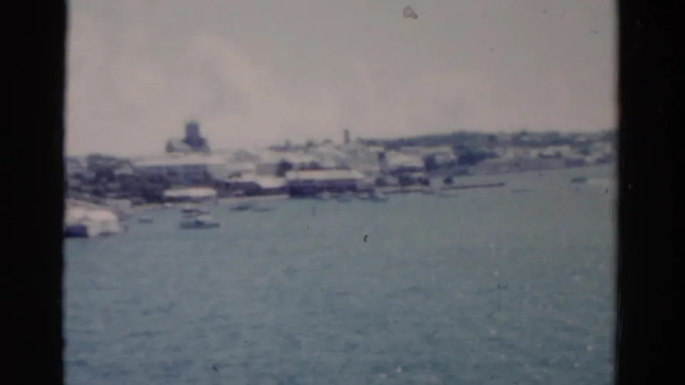 1975 Florida coastal 8mm frame with harbor water, distant boats, and pale waterfront buildings.