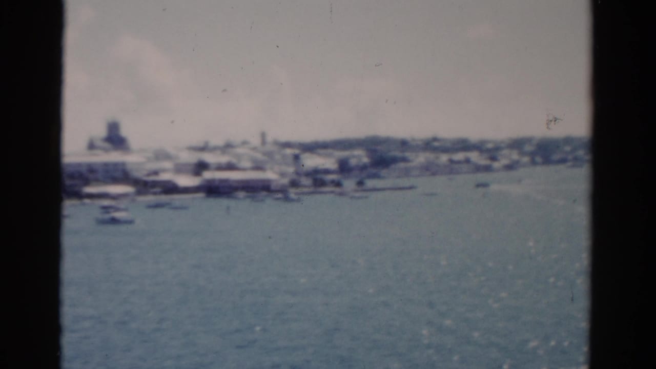 Distant shoreline and small boats across blue water, framed by dark film edges.