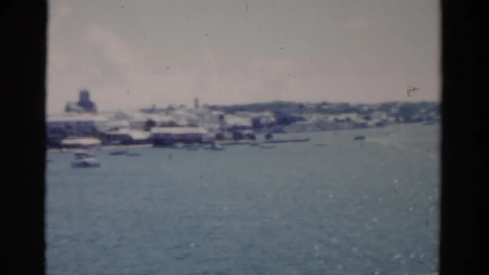 1975 Florida coastal view from a boat, with blue water, small vessels, and a distant developed shoreline in soft 8mm focus.