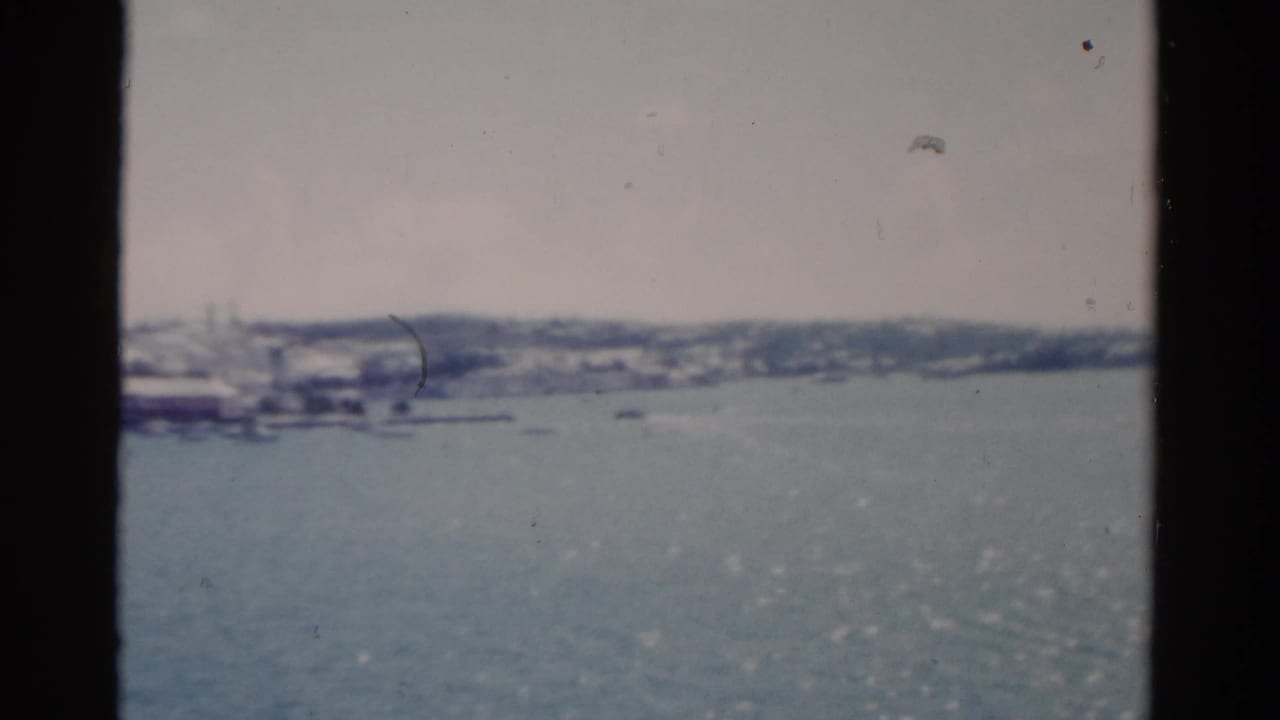 Wide water view with distant shore and small boats under a pale sky.