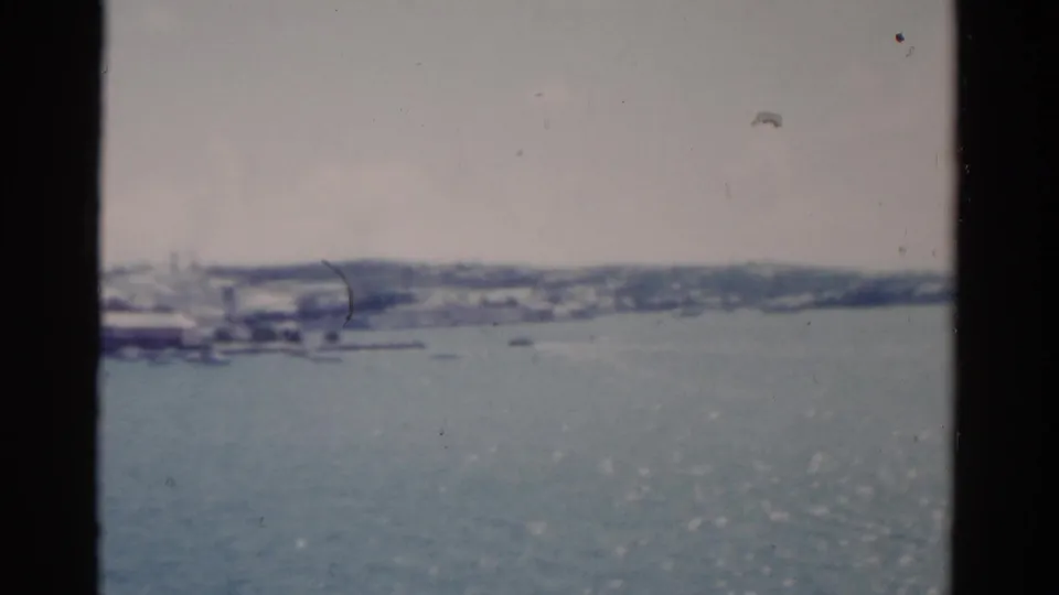 Soft 8mm view of a Florida shoreline from the water, showing scattered boats and low buildings in the distance.