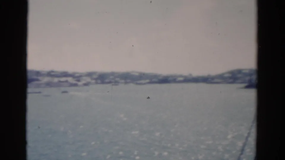 A hazy 1975 Florida waterfront panorama from a moving boat, with glittering water, small boats, and shoreline buildings.