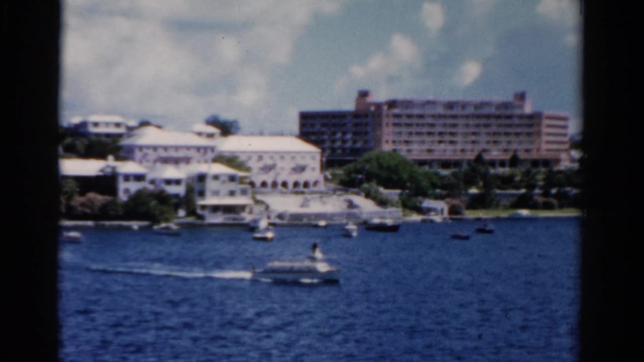 1975 Florida 8mm frame showing a motorboat wake in front of waterfront buildings and a large pinkish hotel.