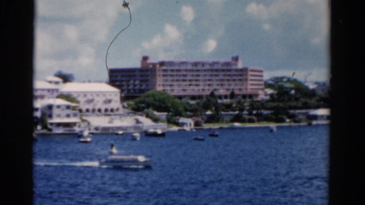 Boat wake on blue water with shoreline hotel and white buildings in the background.