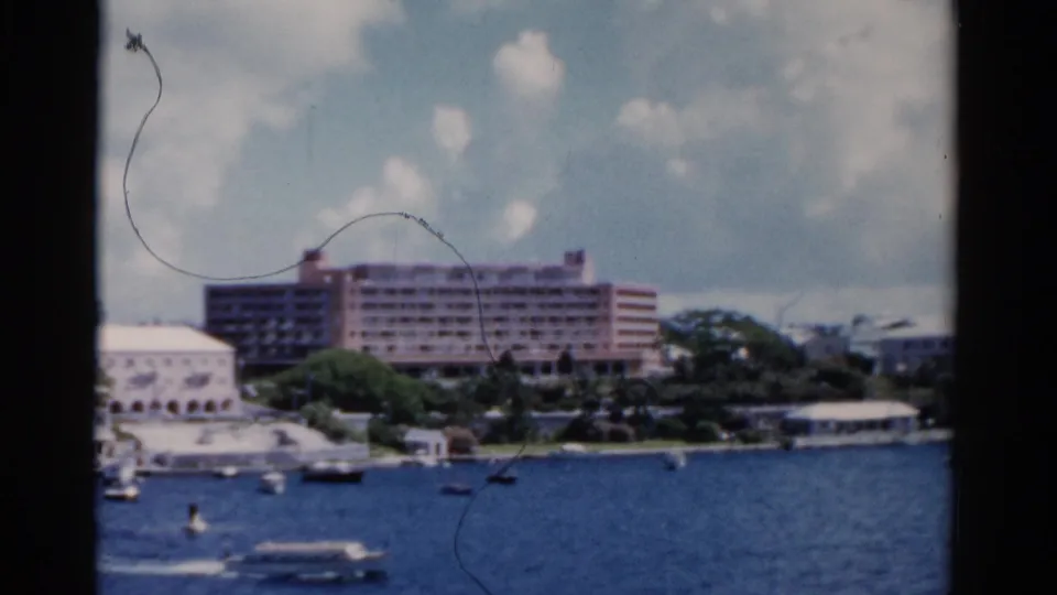 Soft 1975 Florida 8mm frame with a hotel, trees, small boats, blue water, and visible film scratches.