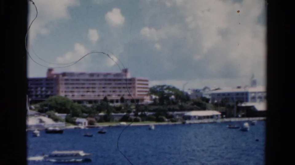 1975 Florida home-movie frame showing boats on blue water below a large shoreline hotel and partly cloudy sky.