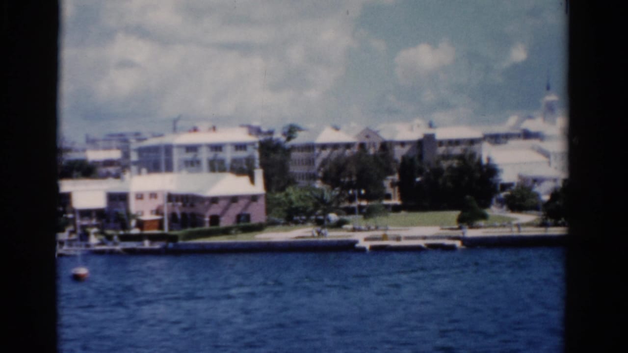 Shoreline buildings, trees, and a small buoy across a blue waterfront.