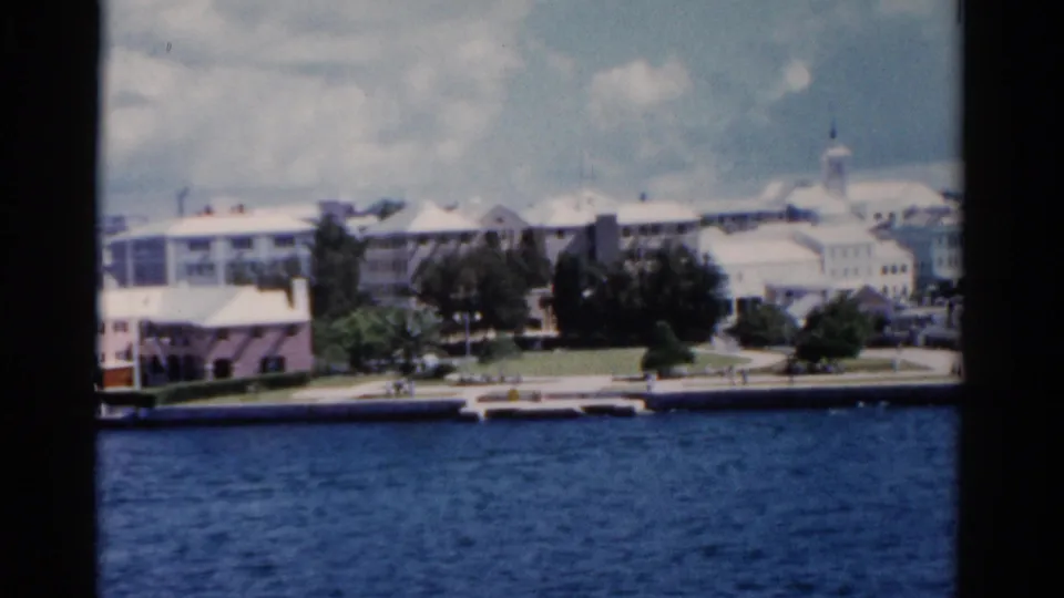 1975 Florida home-movie frame showing a waterfront city from across the water, with trees, low buildings, and a distant domed roof.