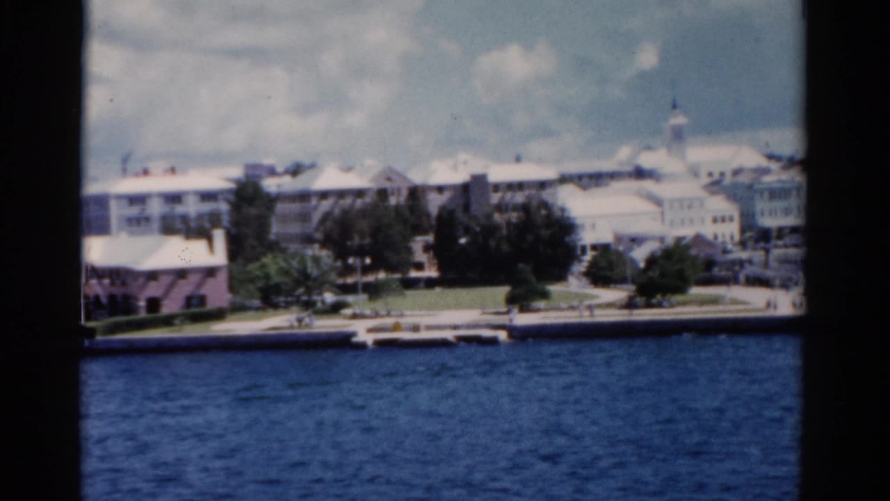 1975 Florida coastal waterfront with blue water, trees, low-rise buildings, and a church steeple seen through a dark frame.