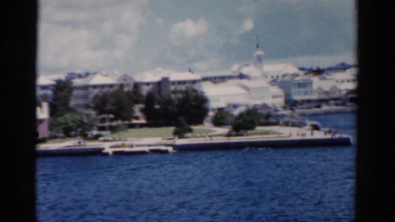 Bright waterfront buildings and trees across blue water, framed by dark vertical edges.