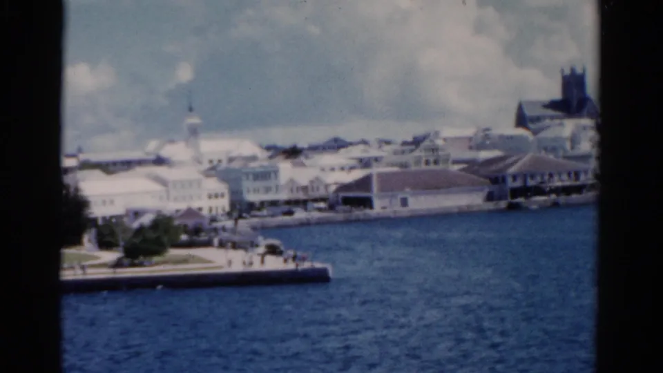 1975 Florida harbor view with blue water, promenade, pale waterfront buildings, a steeple, and a darker tower at the edge of frame.
