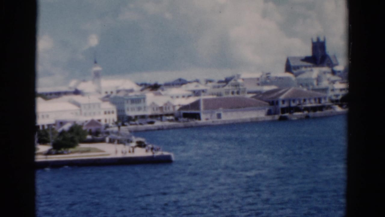 1975 Florida harbor view from the water, showing white waterfront buildings, a pier, and a prominent dark church tower in the skyline.