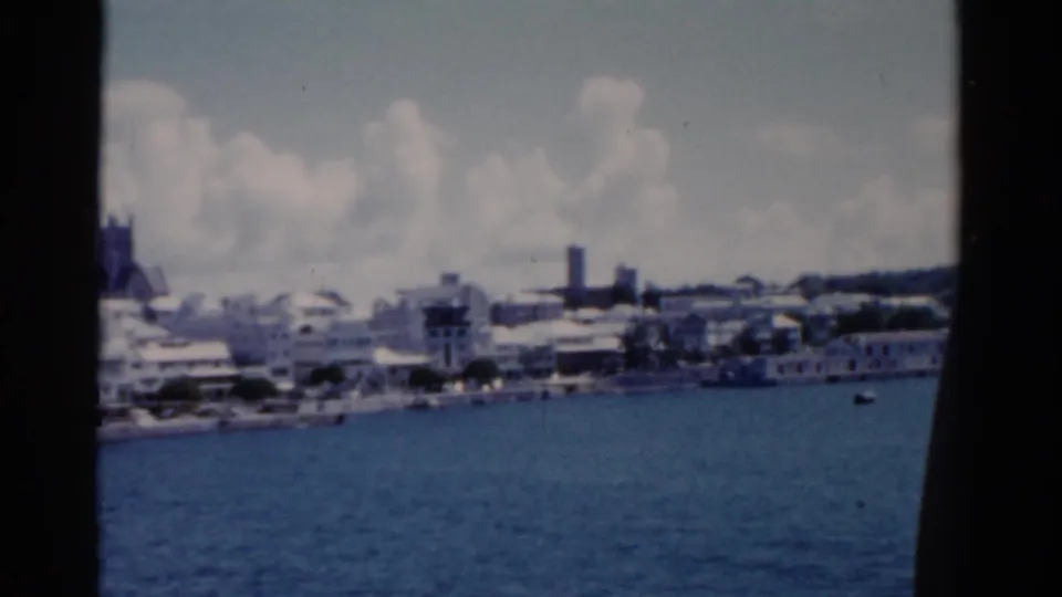 A wider 1975 Florida waterfront view shows low town buildings, a distant church tower, small boats, and open harbor water.