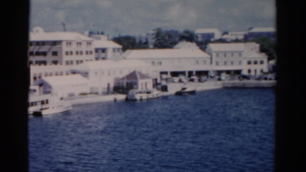 1975 8mm view of pale Florida waterfront buildings and small boats across a harbor on a cloudy day.
