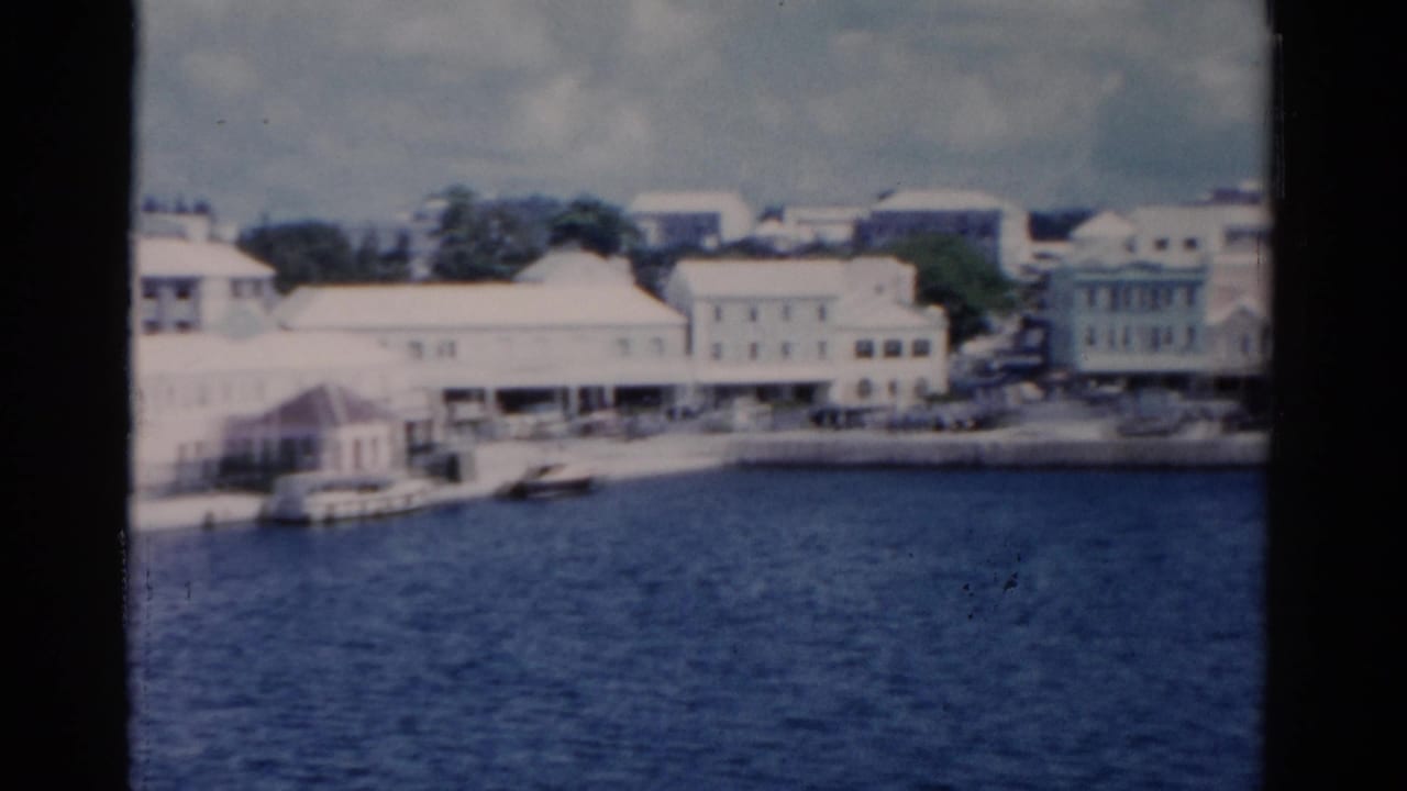 A 1975 Florida harbor view shows light waterfront structures, docked boats, and soft cloudy sky on 8mm film.
