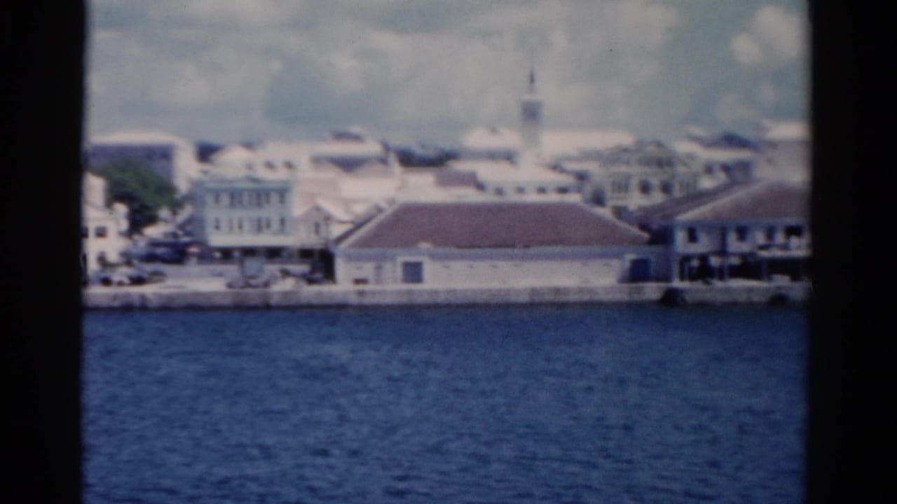 Waterfront buildings and a church steeple seen across blue water from a boat.