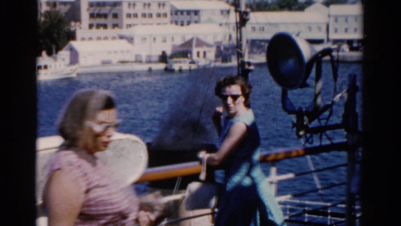 Two adult women on a 1975 Florida boat deck, one in a striped top and one in a blue dress, with waterfront buildings behind them.