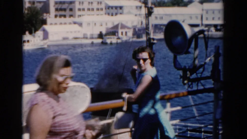 Two adult women on a 1975 Florida boat deck, one in a striped top and one in a blue dress, with waterfront buildings behind them.