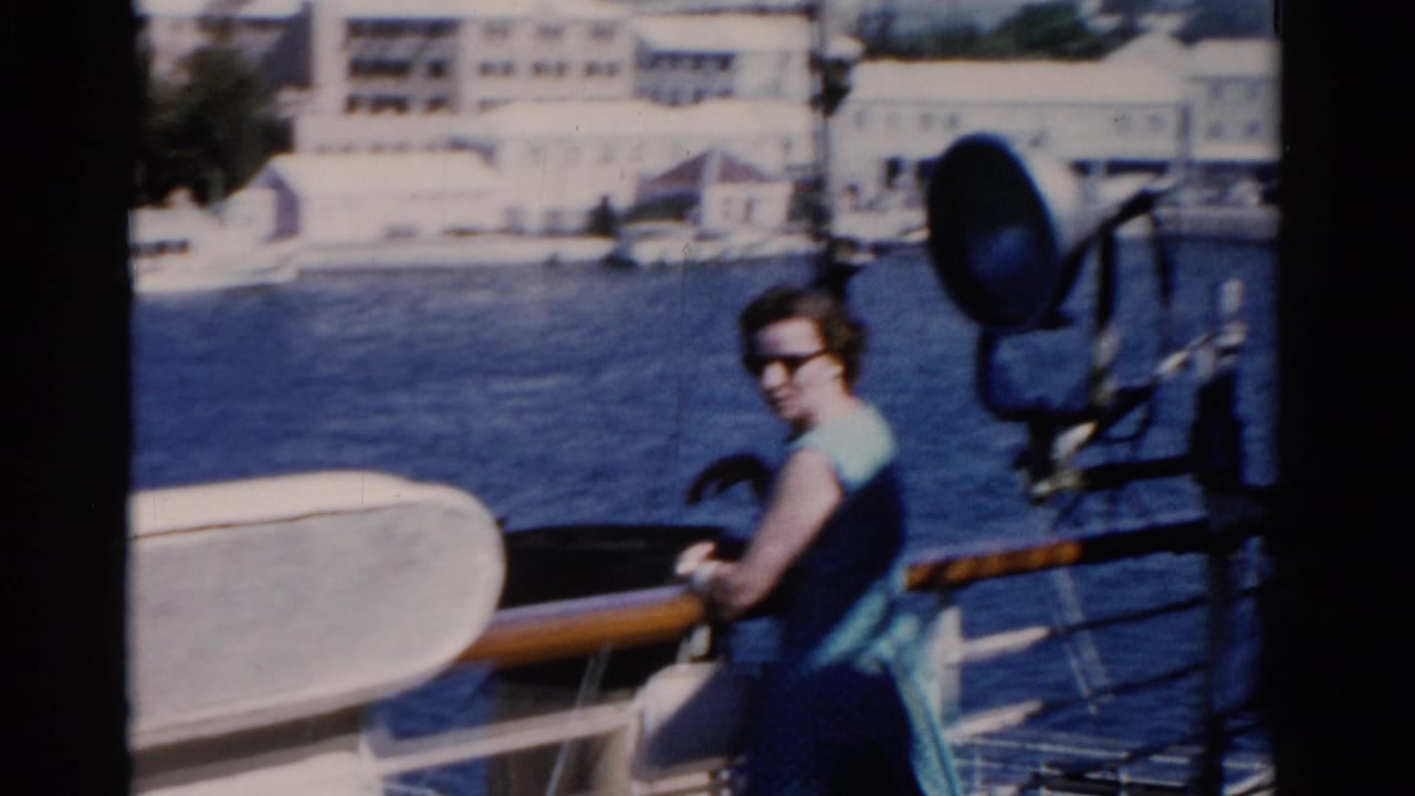 Woman in sunglasses on a Florida ship deck, with a large spotlight, wooden rail, water, and pale waterfront buildings behind her.
