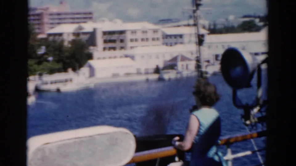 Soft 8mm view of the woman from behind on a ship deck, facing the Florida waterfront across calm water.