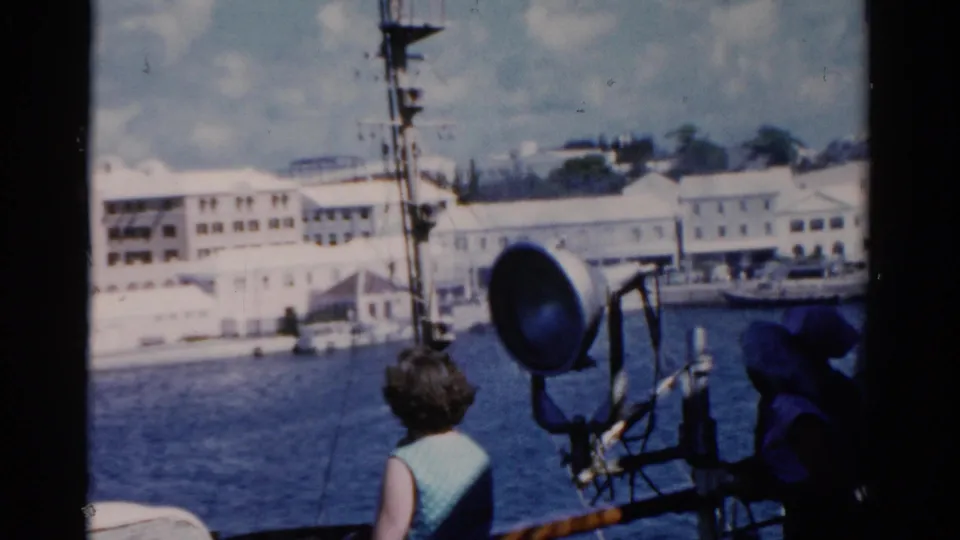 1975 Florida ship-deck view with the woman near a spotlight and rigging, looking toward water and white waterfront buildings.