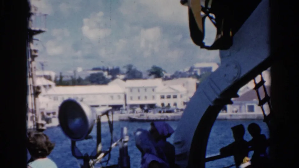 Soft 8mm frame of a Florida waterfront from a ship deck, with a large spotlight and partial view of a passenger near the rail.