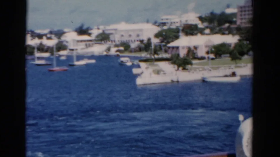 1975 Florida 8mm frame showing sailboats on blue water beside white shoreline buildings and a developed resort waterfront.