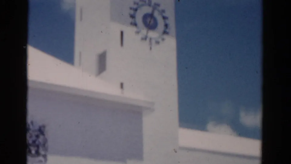 1975 Florida 8mm close-up of a white clock tower facade against blue sky, with soft focus and bright exposure.