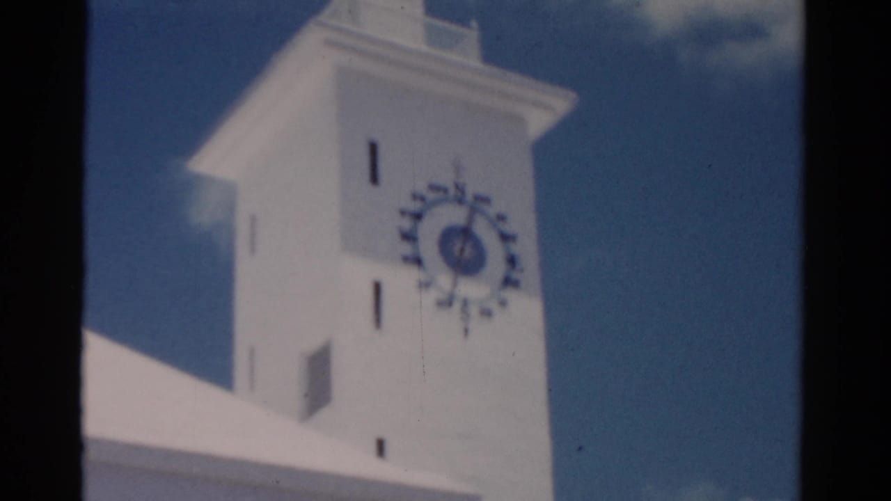 1975 Florida 8mm frame showing a white institutional-looking tower with a prominent clock face and bright blue sky.