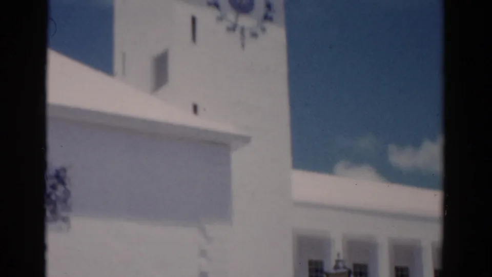 1975 Florida home-movie frame with a white clock tower, upper facade, and dark vertical contact-sheet divider.