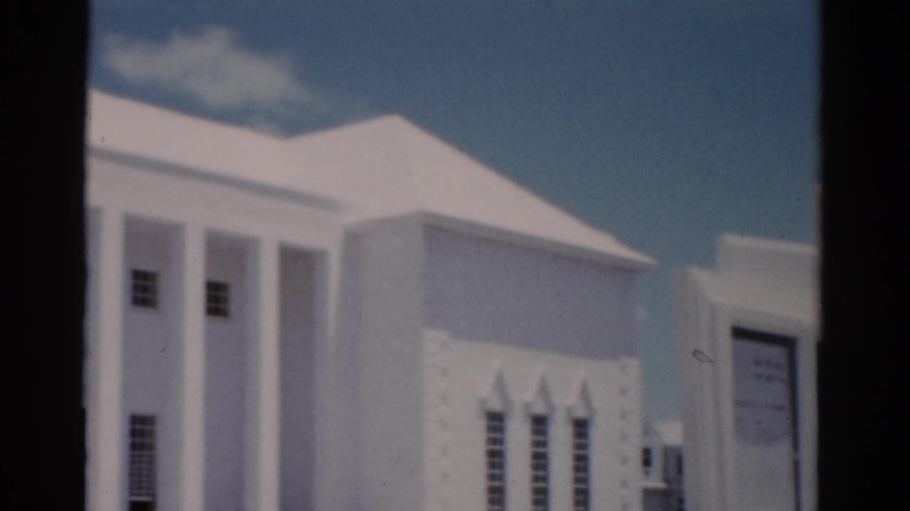 White columned building seen through a dark window frame under blue sky.