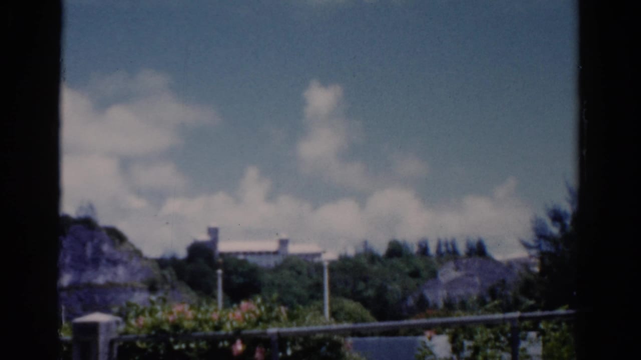 1975 Florida 8mm view of a green hillside, distant white structure, railing, and dark window frame.