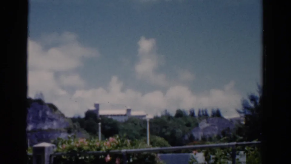 1975 Florida 8mm view of a green hillside, distant white structure, railing, and dark window frame.