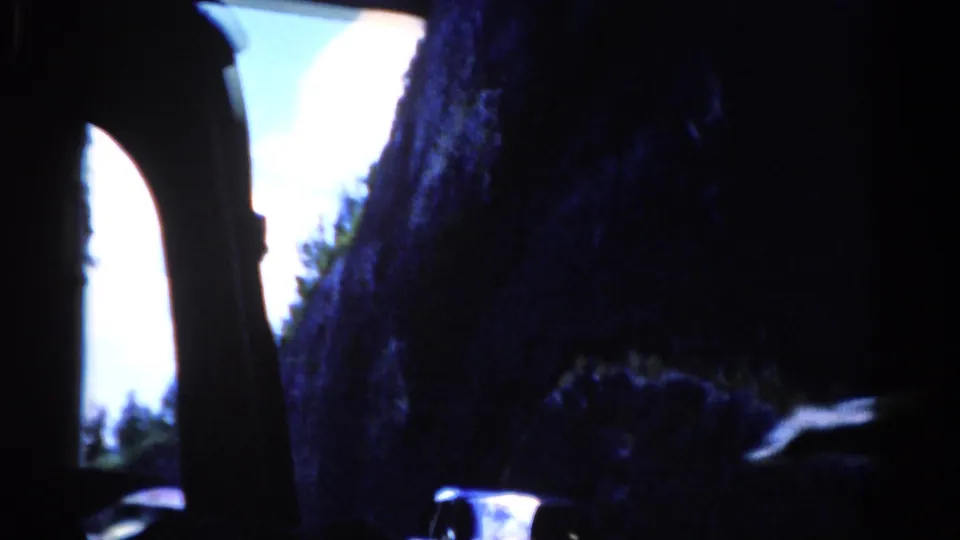 1975 8mm travel footage from Florida showing a shadowed car-window view toward rock walls, sky, trees, and a small vehicle shape below.
