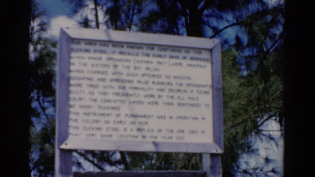 1975 Florida 8mm frame showing a white historical sign in a wooden frame, set against pine trees and blue sky.
