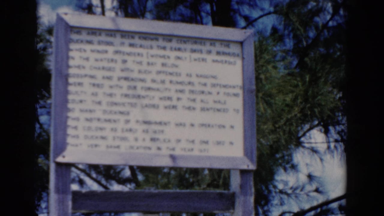 1975 8mm Florida travel frame showing a white wooden historical sign set against pine branches and blue sky.