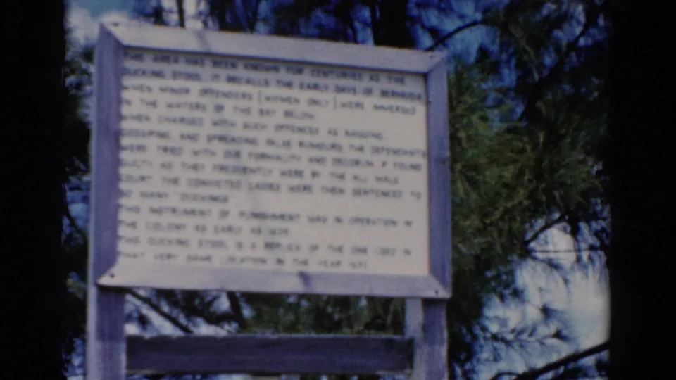 1975 8mm Florida travel frame showing a white wooden historical sign set against pine branches and blue sky.